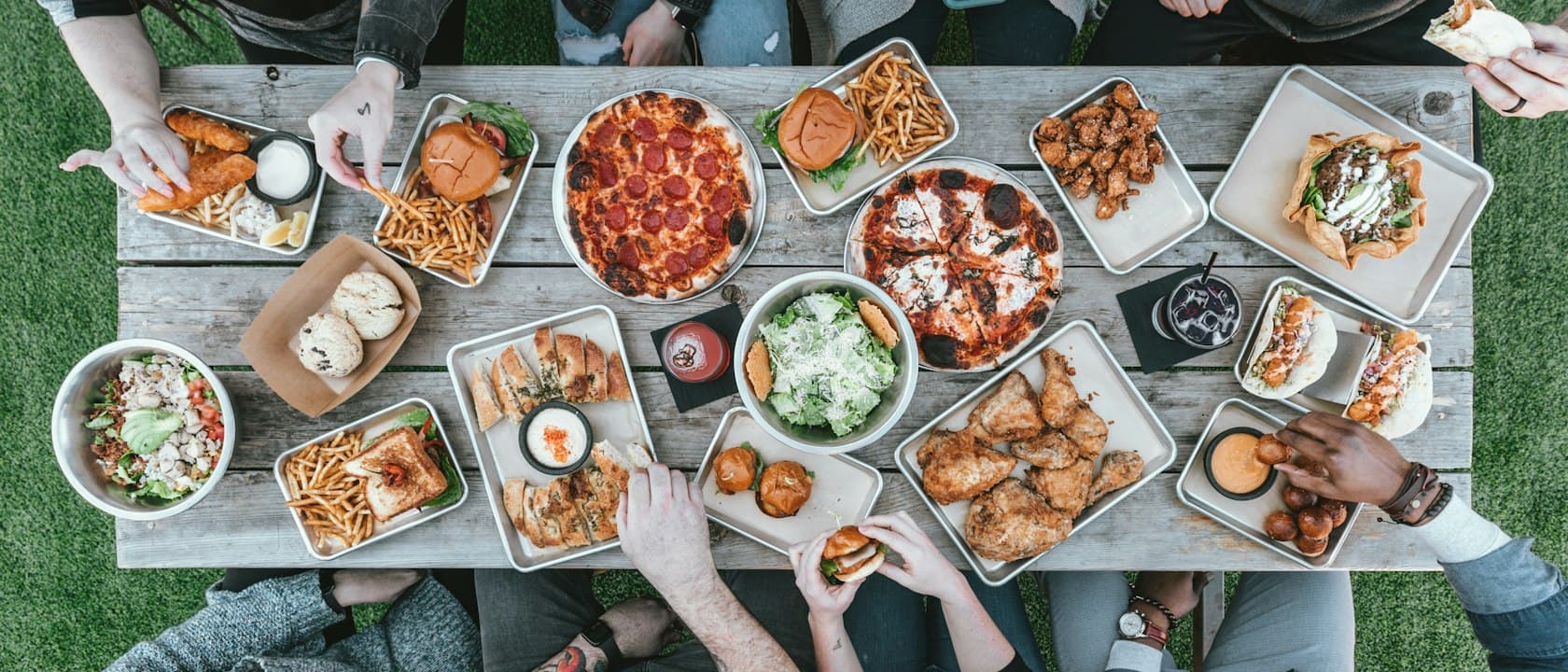 Vue de dessus d'une longue tablée couverte de plats à partager, entourée de convives