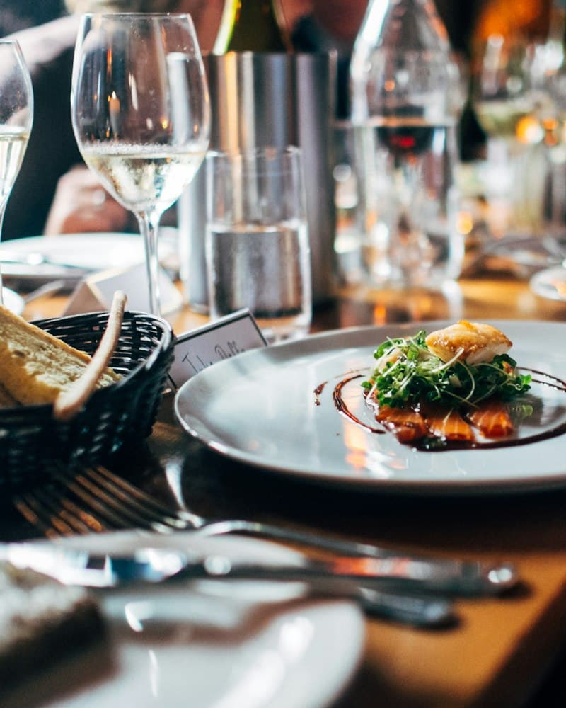 Une assiette dressée posée sur une table de restaurant, entre verres à vin et couverts